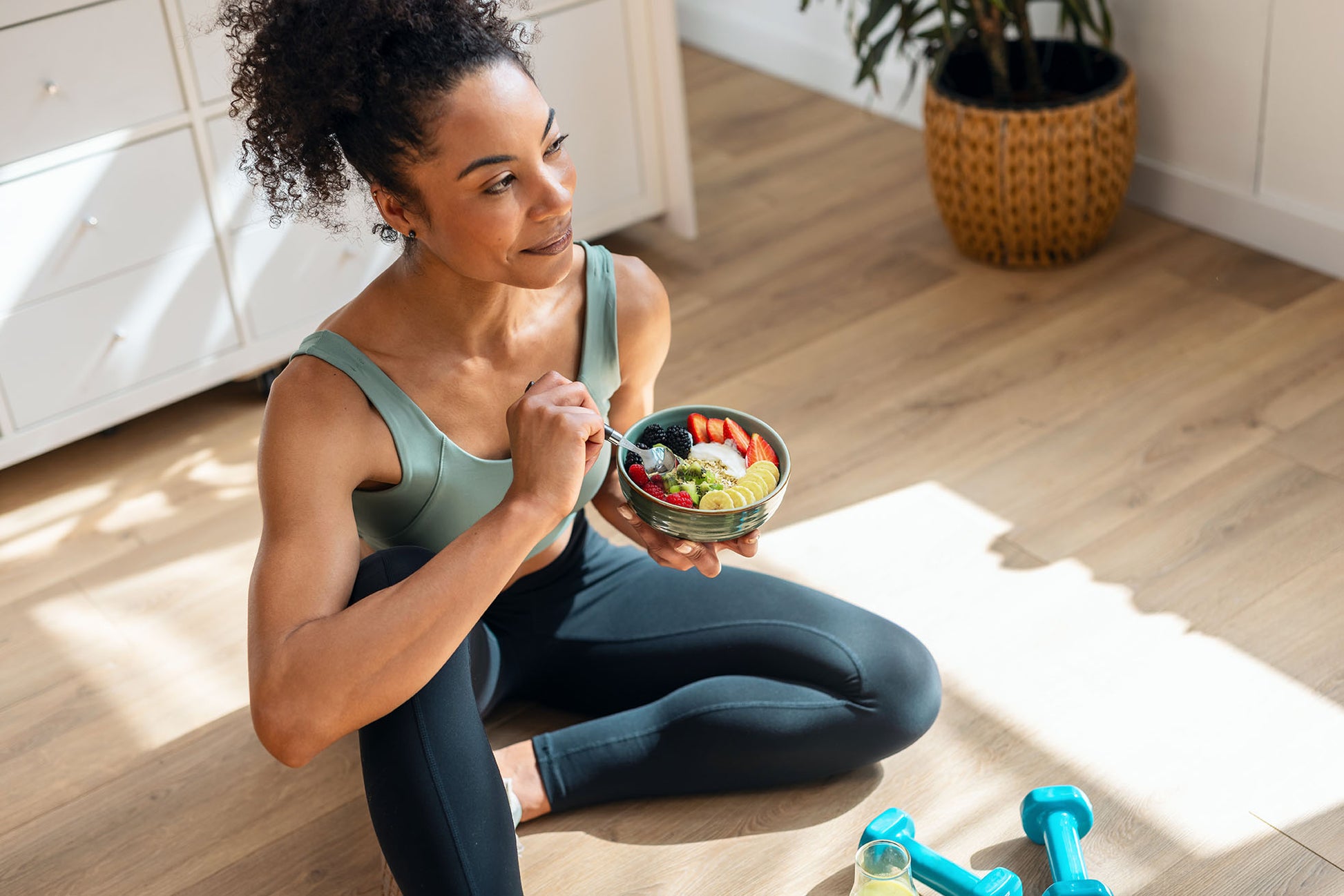 A person in exercise clothes eating a bowl of fruit and yoghurt