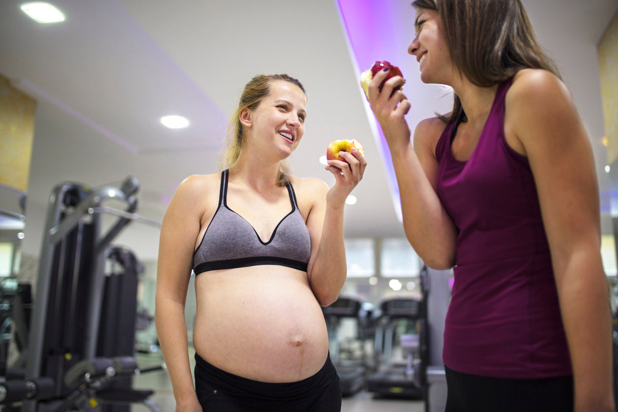 A pregnant woman and her gym instructor eating apples