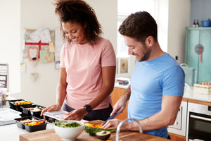 A couple in their gym clothes batch preparing healthy meals in the kitchen