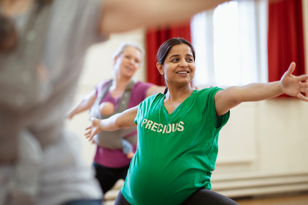 A pregnant woman is doing a yoga stretch in a group class