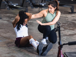 A personal trainer helping a gym goer with a sit up