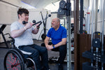 A personal trainer coaching a gym goer in a wheelchair on gym equipment