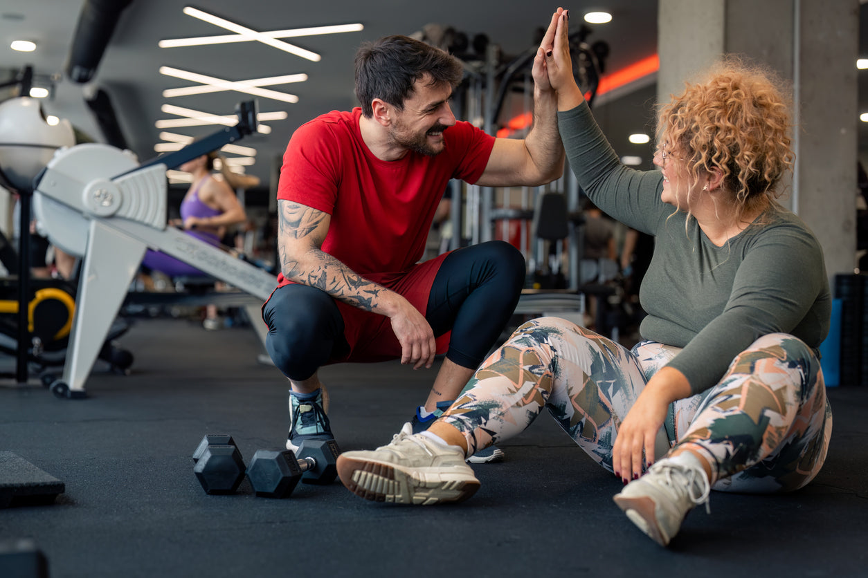 A gym goer sat down and giving a high-five their personal trainer 