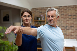 Physical therapist helping a senior man with his shoulder recovery at home