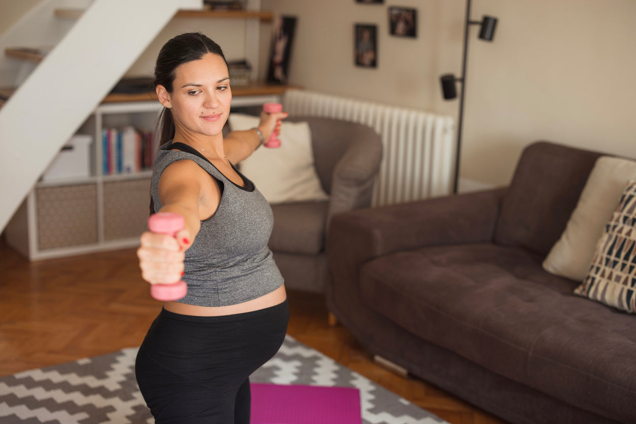 A pregnant woman exercising in her living room in a warrior yoga position