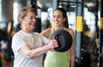 A gym instructor helping a gym goer with their technique lifting a kettlebell