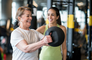 A gym instructor helping a gym goer with their technique lifting a kettlebell