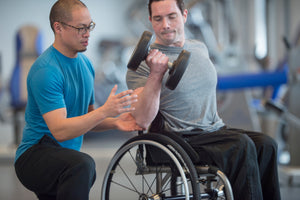 A personal trainer helping a person in a wheelchair with weight lifting