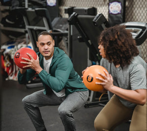 A personal trainer showing their client how to squat with a weighted ball